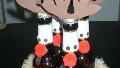 Eine Gruppe von Bierflaschen, dekoriert mit einem Geweih aus Pappe und roten Pompons, sitzt in einem geflochtenen Korb.