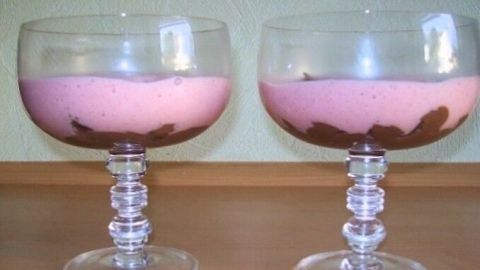 Zwei Dessertgläser zeigen eine Mousse au Chocolat mit fruchtigem Sektschaum, elegant auf einem Holztisch serviert.