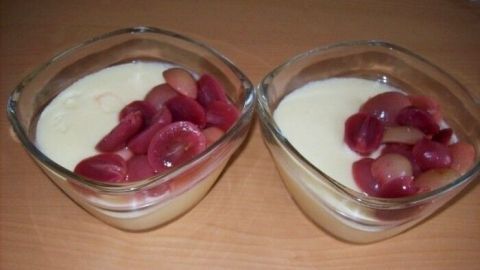 Zwei Schalen mit cremigem Weißwein-Dessert, garniert mit frischen Trauben, auf einem Holztisch angerichtet.