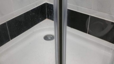 Eine Glas-Duschkabine mit Kalkablagerungen wird in einer Dusche betrachtet, um sie mit Nassschleifpapier zu reinigen.