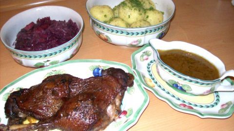 Saftige Gänsekeulen in Rotweinsoße garnieren einen Tisch, umgeben von Beilagen wie Kartoffeln und Rotkohl.