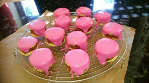 Kleine runde Punschkrapferl mit pinker Glasur stehen auf einem Rost zum Abkühlen in einer hellen Umgebung.