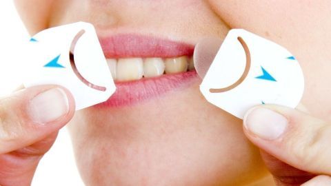Eine Frau hält zwei kleine Aufkleber an ihren Lippen, um Herpes zu behandeln, während sie in einem hellen Raum steht.