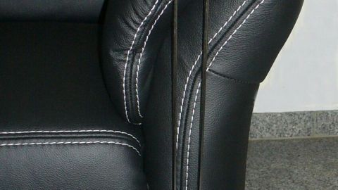 Ein schwarzes Sofa mit einem Kratzschutz, der an der Sofakante befestigt ist, um das Kratzen am Sofa unauffällig zu verhindern.