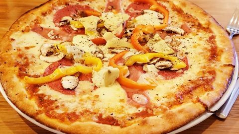 Eine leckere Quark-Öl-Pizza liegt auf einem Teller, belegt mit Schinken, Paprika und Käse, bereit zum Genießen.