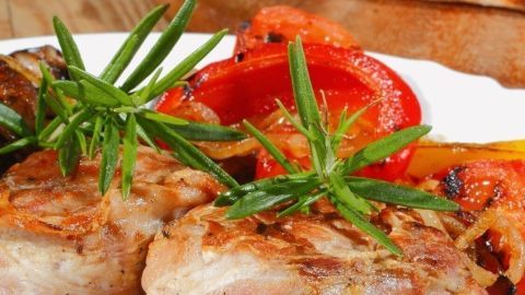 Zwei saftige Räuberbraten auf einem weißen Teller, umgeben von buntem Gemüse und frischen Kräutern, auf einem Holztisch.