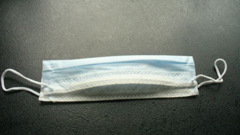 Eine medizinische Maske liegt flach auf einer dunklen Oberfläche, bereit zum Einsatz, um die Nase vor Kälte zu schützen.