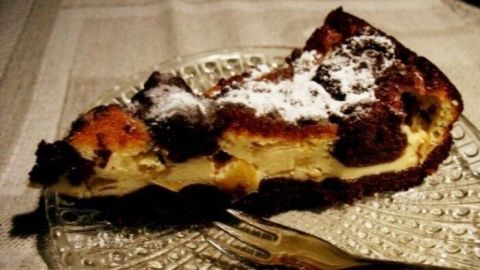 Ein Stück Zupftorte liegt auf einem dekorativen Glas-Teller, bestäubt mit Puderzucker, neben einer Gabel im gedämpften Licht.