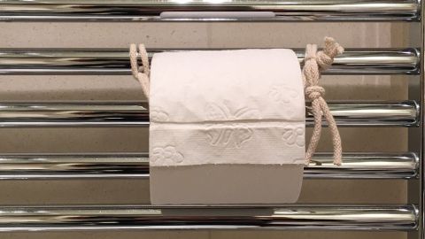 Ein Toilettenpapier-Halter hält eine Rolle in einem kleinen Bad, umgeben von modernen Fliesen und glänzenden Stangen.