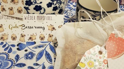 Ein dekorativer Teekessel steht neben einer Tasse auf einem blühenden Tischdeckenmuster, umgeben von hübschen Teebeuteln.