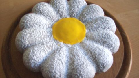 Eine blumenförmige Backform zeigt einen bunten Blumenkuchen mit gelbem Zentrum und weißen Blütenblättern.
