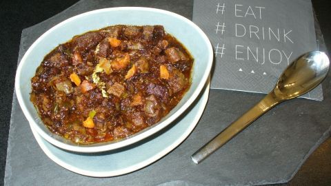Ein reichhaltiges Ragout vom Ochsenschwanz in einer weißen Schüssel, angerichtet auf einem schwarzen Untergrund neben einem Löffel.