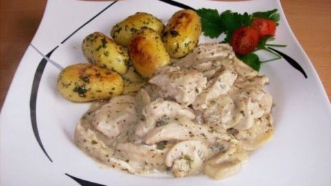 Saftiges Hähnchen-Filet liegt cremig angerichtet auf einem Teller, umgeben von goldbraunen Kartoffeln und frischen Kräutern.