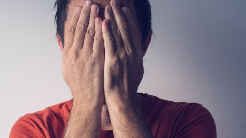Eine Person mit Händen vor dem Gesicht zeigt eine Reaktion auf Fremdschämen in einem neutralen Hintergrund.