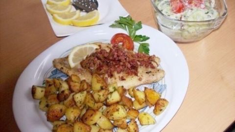 Das Rotbarsch-Filet Finkenwerder Art liegt auf einem Teller mit knusprigen Kartoffeln und einem Salat neben Zitronenscheiben.