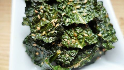 Grüne Kale Chips liegen knusprig auf einem weißen Teller und warten darauf, genossen zu werden.