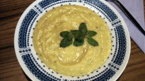 Eine cremige Steckrüben-Suppe liegt in einem dekorativen Teller, garniert mit frischen Kräutern, auf einem Holzuntergrund.