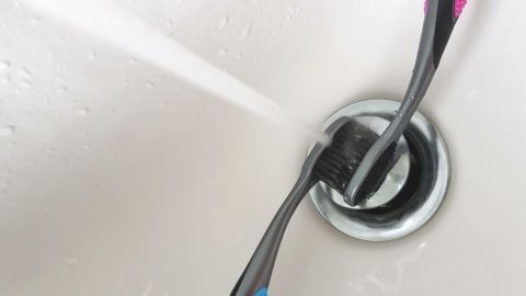 Eine Zahnbürste wird unter Wasser gereinigt, während sie in einem Waschbecken steht, um Hygiene zu gewährleisten.