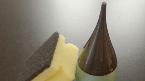 Ein eleganter Flakon mit Geschirrspülmittel steht neben einem Schwamm auf einer dunklen Oberfläche, bereit zum Reinigen.