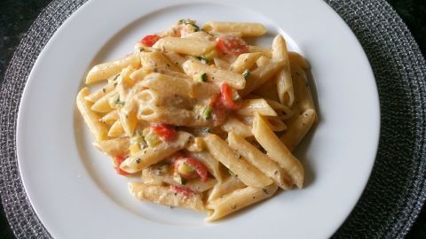 Zucchini-Carbonara wird auf einem weißen Teller serviert, mit Sahnesauce und Tomaten, auf einem dunklen Tischuntergrund.