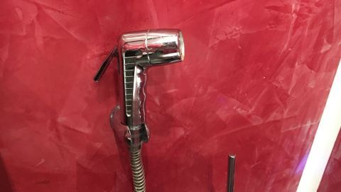 Eine glänzende Toilettendusche ist an einer roten Wand montiert und bereit, zur Reinigung verwendet zu werden.