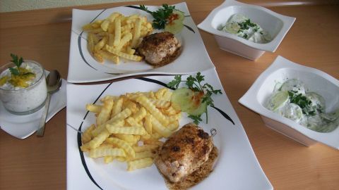 Zwei Teller mit gefüllten Schweinesteaks und Pommes frites, daneben köstlicher Joghurt-Dip in Schalen.