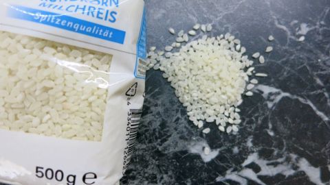 Eine Packung Rundkornmilchreis liegt offen auf einem Marmoruntergrund, etwas Reis ist daneben verstreut. Text: "Spitzenqualität, 500 g".