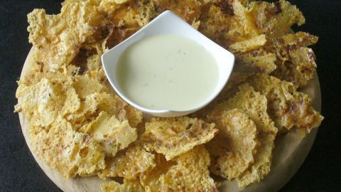 Käsechips sind knusprig und goldbraun, serviert auf einem Holzbrett mit einer kleinen Schüssel Dip in der Mitte.