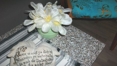 Eine Vase mit weißen Tulpen steht auf einem gemusterten Tisch, umgeben von einem dekorativen Stein im Raum.