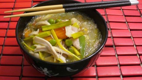 Eine schwarze Schüssel mit asiatischer Hühnersuppe, gefüllt mit frischem Gemüse und Hühnerfleisch, liegt auf einem roten Tisch.