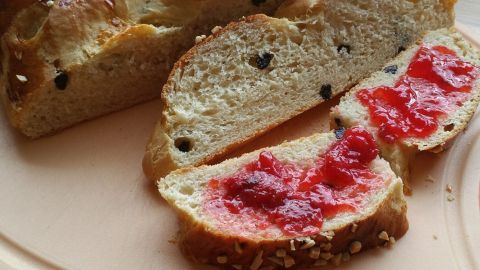 Ein weicher Hefezopf liegt auf einem Teller, dekoriert mit Schmand und frisch zubereiteter Marmelade in einem Glas.