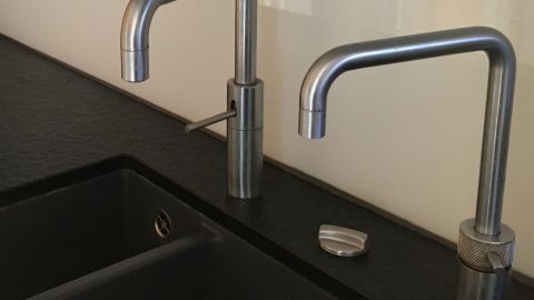 Zwei Wasserhähne stehen über einem dunklen Waschbecken und sind bereit, heißes Wasser bereitzustellen.