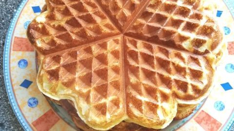 Auf einem Teller liegen mehrere knusprige, goldbraune Waffeln. Sie sind zart und appetitlich angerichtet, umgeben von einem beige-braunen Tisch.