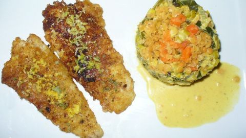 Knusprig panierte Kabeljaufilets liegen neben einem bunten Gemüserisotto, umgeben von einer Sauce.