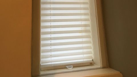 Ein schmaler Kastenfenster mit hellen Jalousien schützt vor Wärmeverlust in einem Raum mit neutralen Wänden.