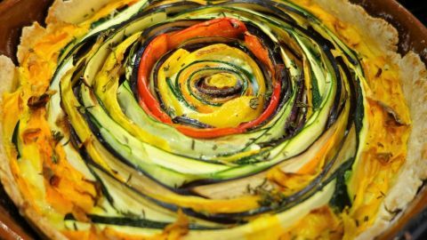 Eine farbenfrohe Gemüse-Spiral-Tarte liegt in einer runden Form und zeigt spiralförmig angeordnete, frische Gemüsestreifen.