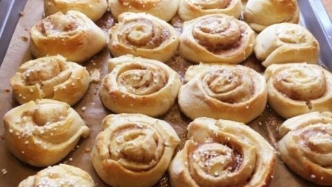 Zimtschnecken liegen frisch gebacken auf einem Blech, umgeben von braunem Pergamentpapier in einer gemütlichen Küche.