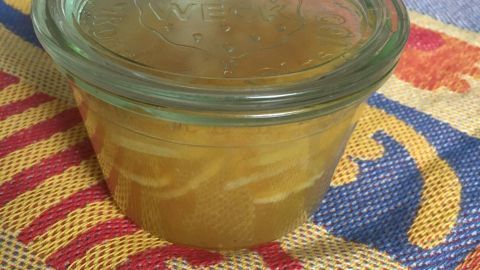 Ein Glas mit lemonfarbener Lemon Curd steht auf einem bunten Tischset. Der Hintergrund ist einfach und hell.