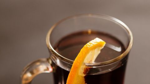 Ein Glaskrug enthält Rotweinpunsch mit einer Orangenscheibe oben, auf einem dunklen Tisch präsentiert.