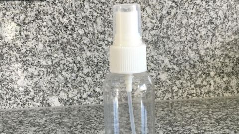 Eine Sprühflasche mit der Beschriftung "Brille" steht auf einer grauen Arbeitsplatte, bereit zum Reinigen von Brillen.