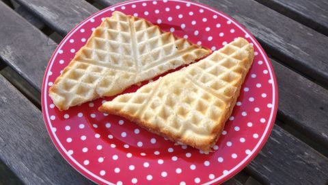 Zwei Waffeln, golden-braun und knusprig, liegen auf einem roten Teller mit weißen Punkten und warten darauf, genossen zu werden.