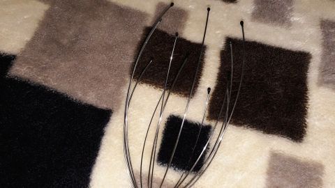 Eine Hand hält einen Haarrechen aus Metall über einem gemusterten Teppich, ideal für Tipps, um schnell längere Haare zu bekommen.