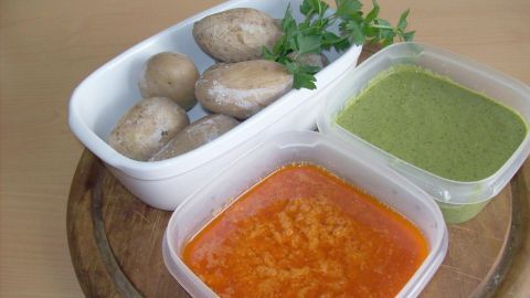 Papas arrugadas liegen zusammen mit Mojo rojo und Mojo verde auf einem Holzbrett, bereit zum Servieren.