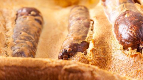 Wurststücke liegen in einem goldenen, aufgeblähten Teig in einem Ofen, was ein traditionelles Gericht namens Toad in the Hole zeigt.