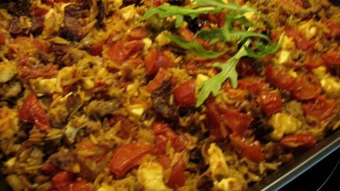 Ein Auflauf aus Hackfleisch und Nudeln ist goldbraun gebacken, garniert mit frischen Tomaten und Kräutern.