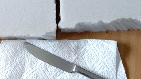 Zwei große Schaumstoffstücke liegen auf einem Tisch, während ein Messer und eine Flasche Öl daneben bereitstehen.