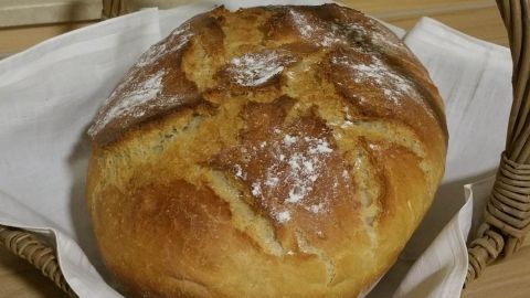 Ein frisch gebackenes Dinkel-Roggenbrot liegt in einem Korb, umgeben von einem weißen Tuch auf einer Holzoberfläche.