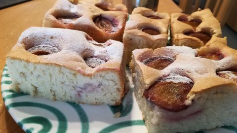 Ein Obstkuchen mit Eiweiß-Resten liegt auf einem grünen Teller, dünn mit Puderzucker bestreut und teils angeschnitten.