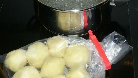Eine Tüte mit gefrorenen Kartoffelknödeln liegt neben einem kochenden Topf auf dem Herd, bereit zum Kochen.