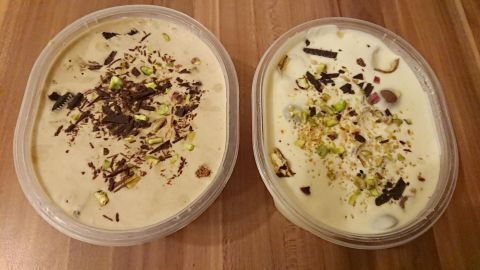 Zwei Schalen mit selbstgemachtem Baileyseis, dekoriert mit Schokolade und Nüssen, auf einem Holzuntergrund platziert.